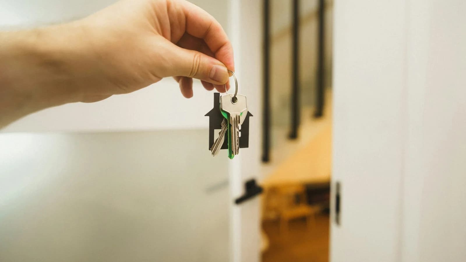 Hand holding a set of house keys on a house-shaped keyring, ready to hand over to a tenant