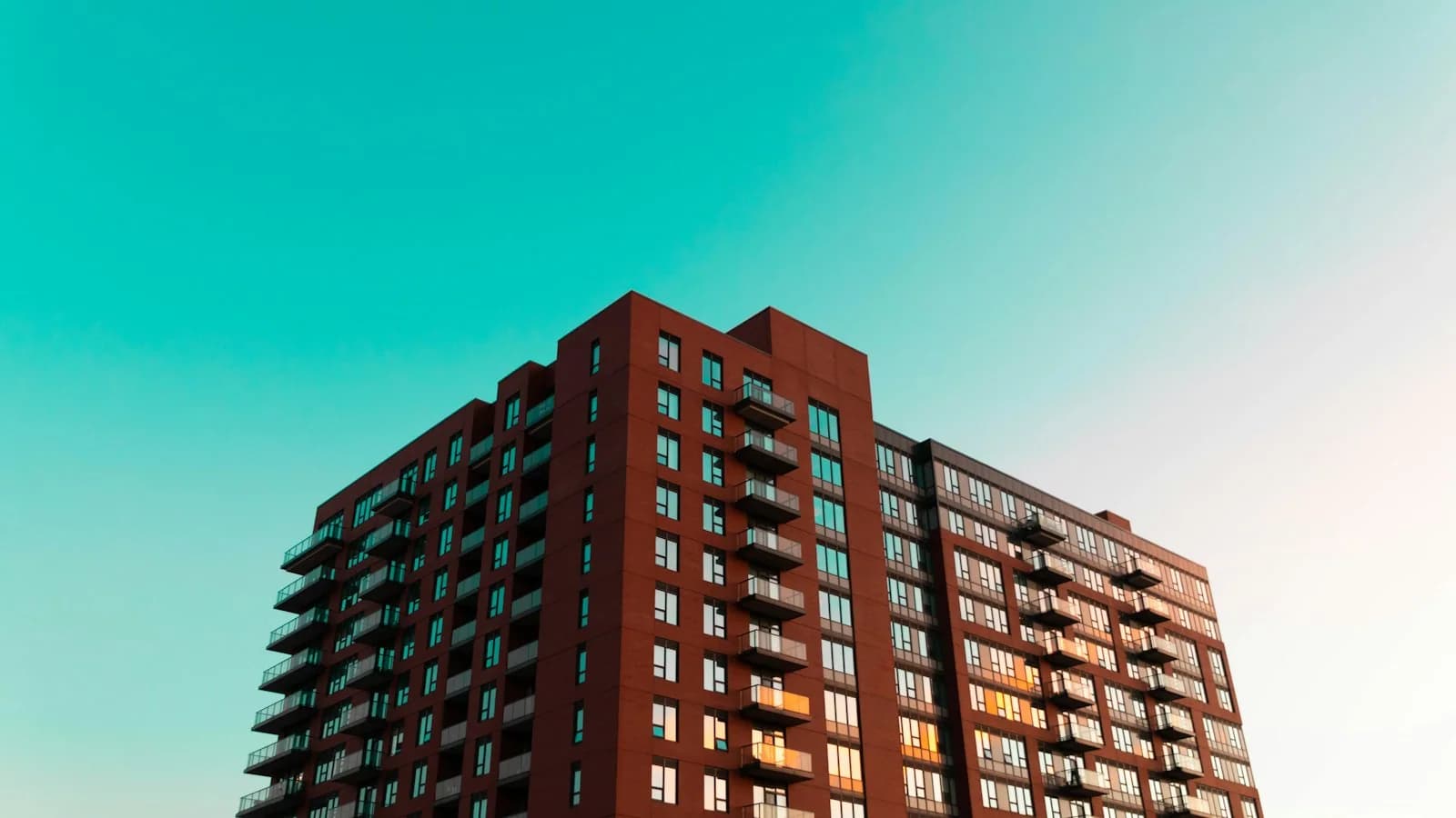 Red-brick apartment building with rows of balconies against a clear blue sky