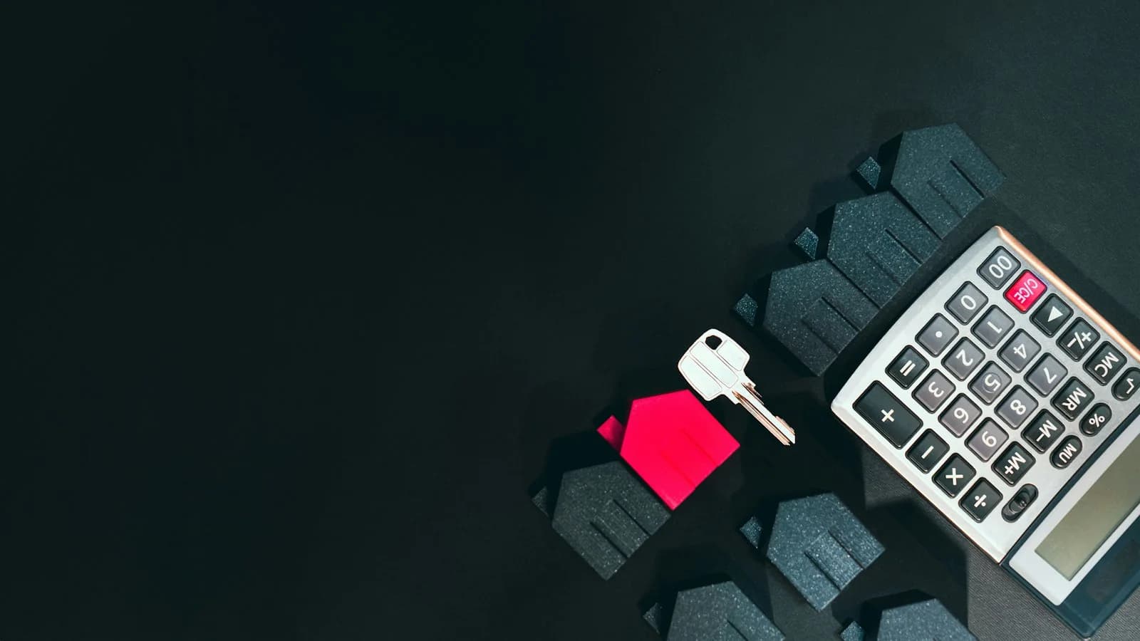 Small house models, a silver key and a calculator on a dark surface
