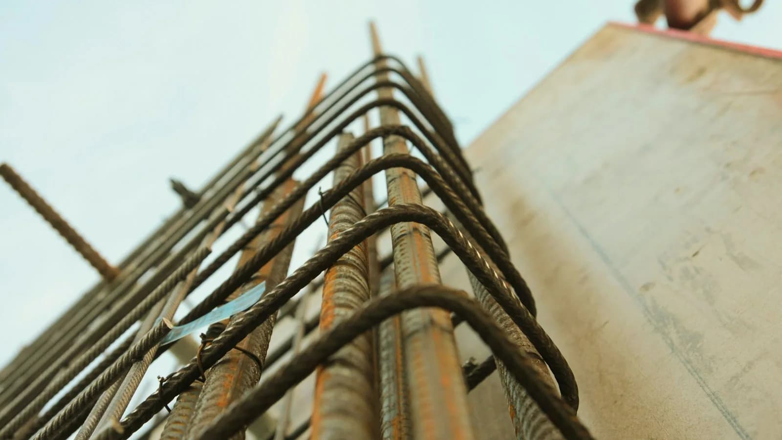 Low-angle view of steel reinforcement bars with closed ties rising beside a concrete column on a building site